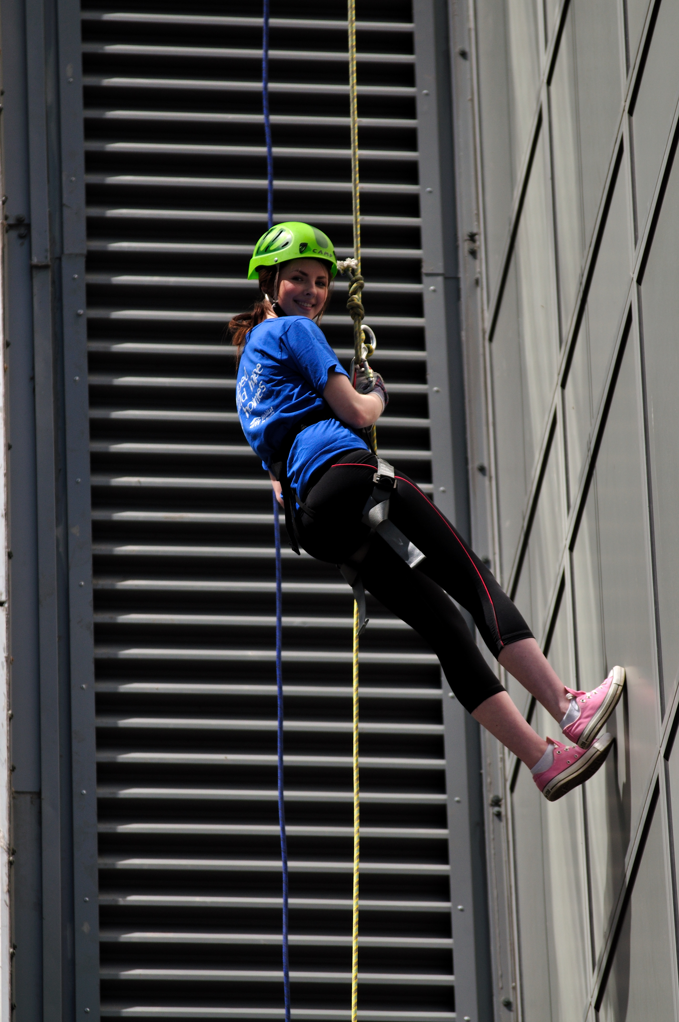 A volunteer abseil down the side of a building, smiling to camera