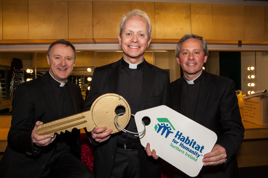 The musical group 'The Priests' holding a large foam key with Habitat's logo on it