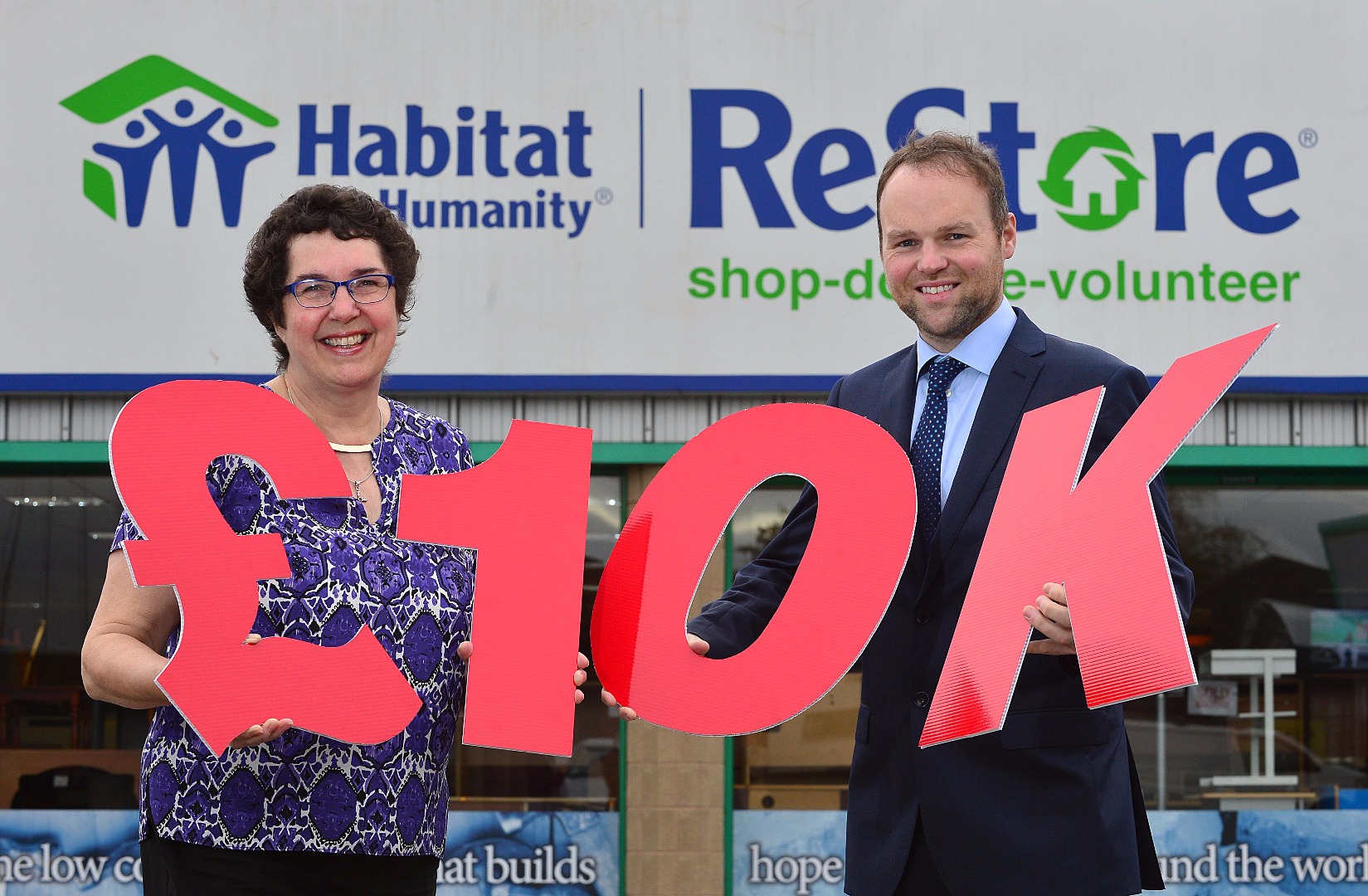 Chief Executive of Habitat Ireland Jenny Williams and Managing Director of CTS Projects Connaire McGreevey outside Habitat ReStore Lisburn, holding large red letters which say '£10K'