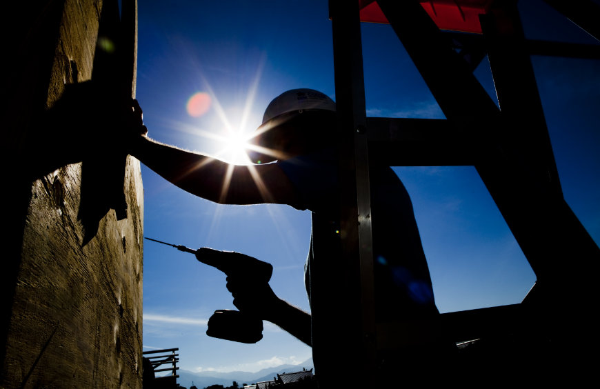 The silhouette of a Habitat volunteer holding a drill, the sun is in the background 