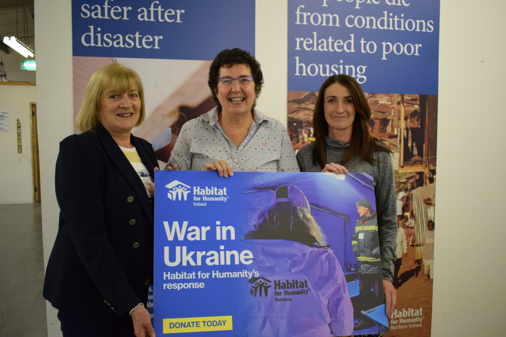 Jenny Williams, Habitat Chief Executive (center) with members of Downshire Tennis Club. They all all holding a sign which says "War in Ukraine" with a photo of Habitat's Ukraine Response